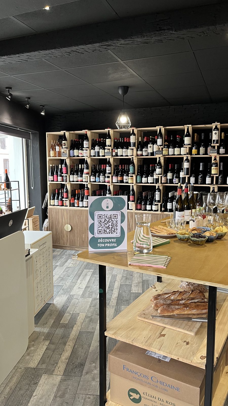 La cave En Bouteille : le mur de bouteilles et la table de dégustation avec sa planche